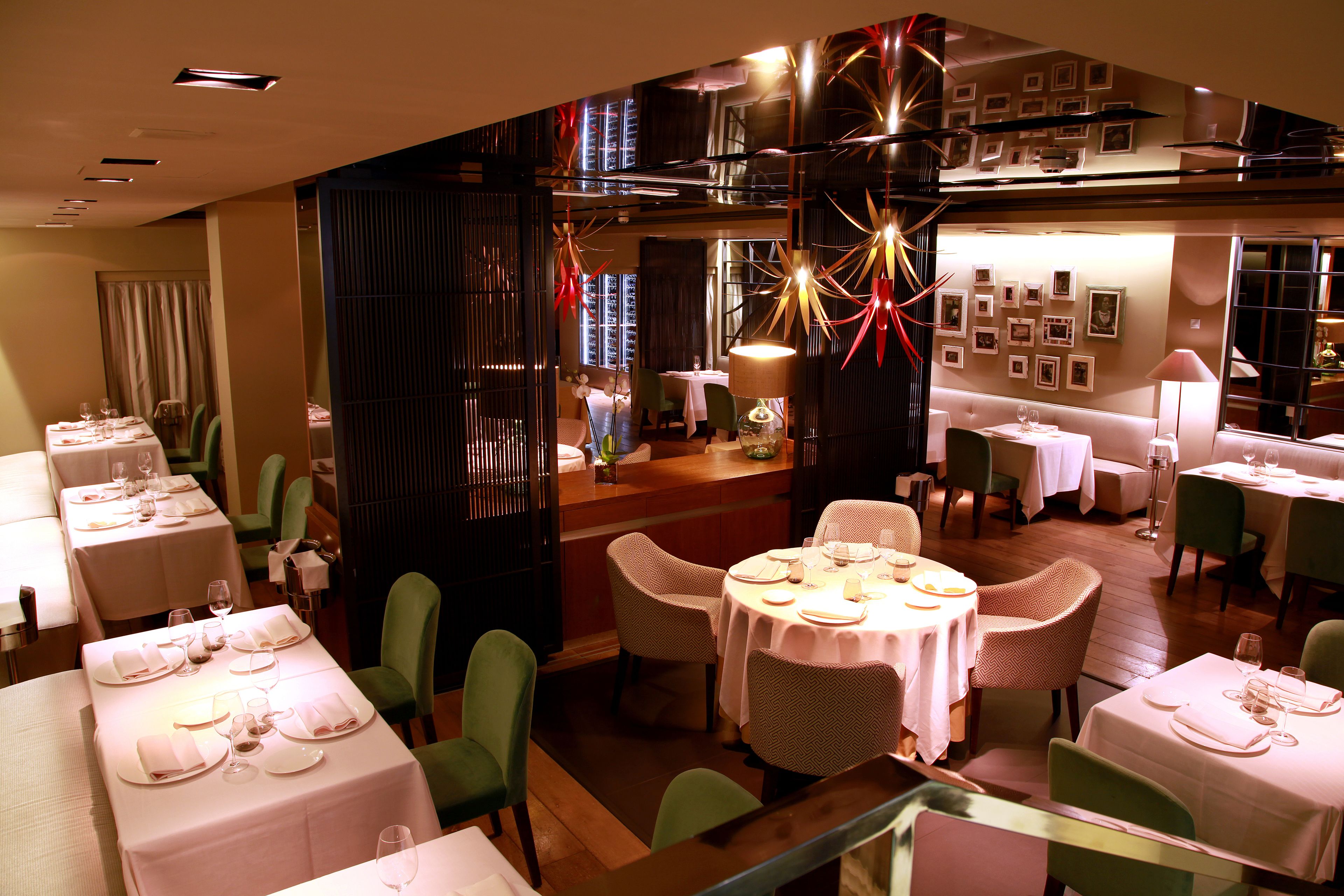 A restaurant with multiple dining tables, green chairs, and a modern interior design.