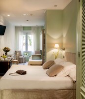 Habitación de hotel con cama, mesita de noche, lámpara y vista al exterior a través de la ventana.