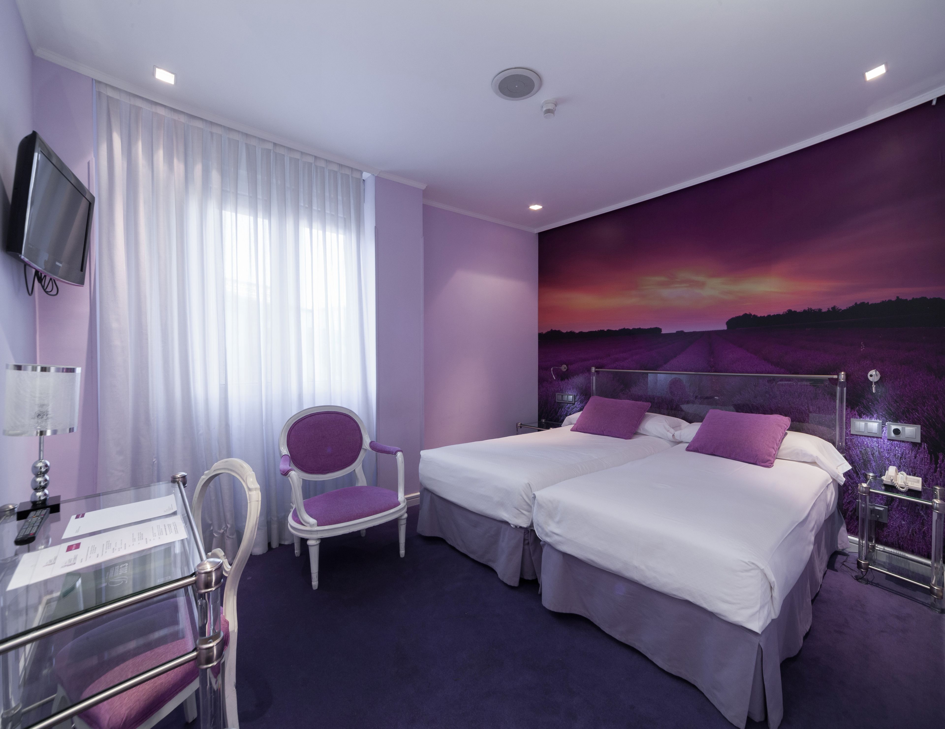 A hotel room with two beds, a chair, a desk with a computer, and a TV.