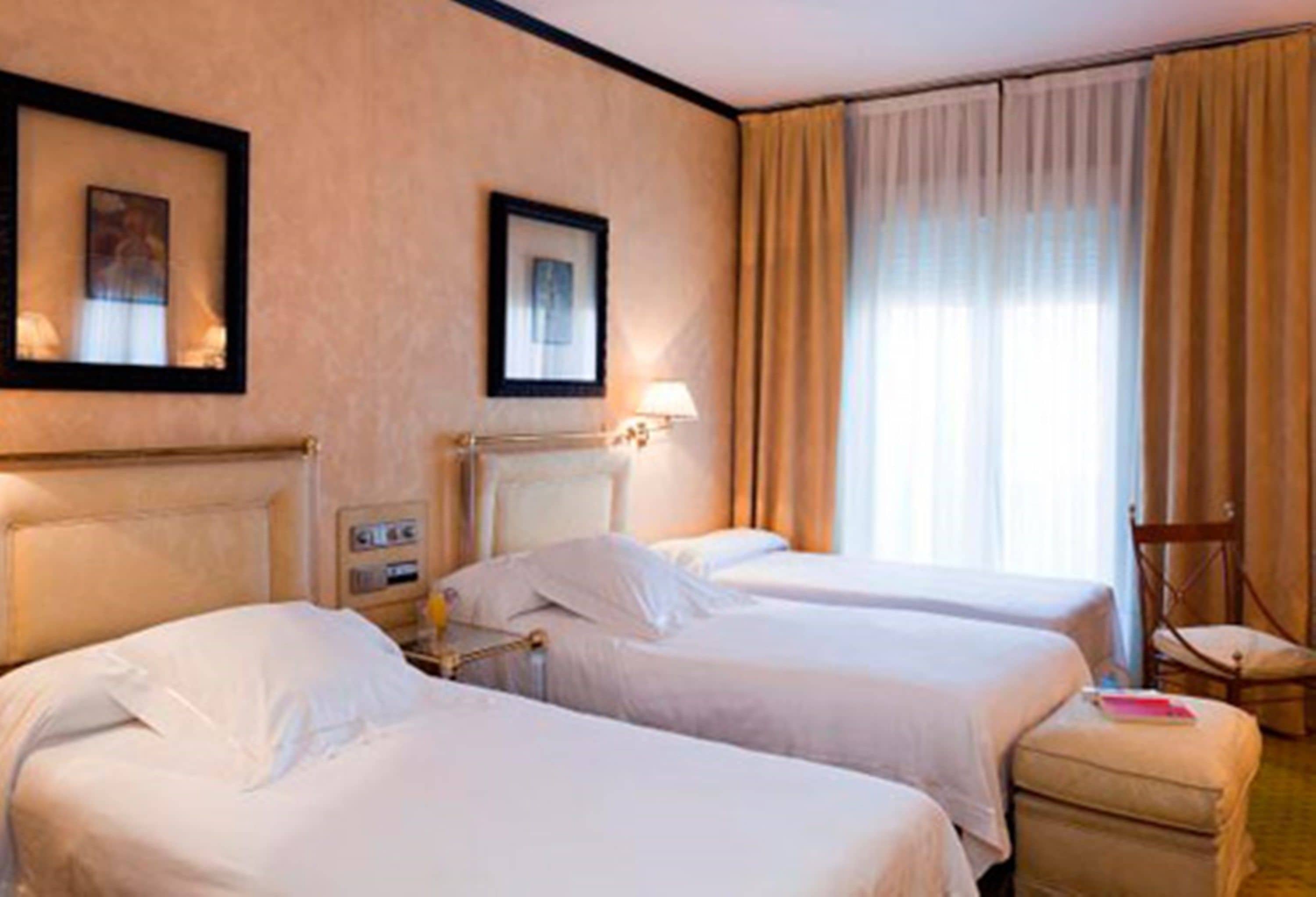 A hotel room with two beds, a chair, and a window with curtains.