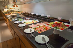 En buffet med et bredt udvalg af mad, herunder salater, kød og grøntsager, præsenteret på en lang bordplade med serveringsbestik.