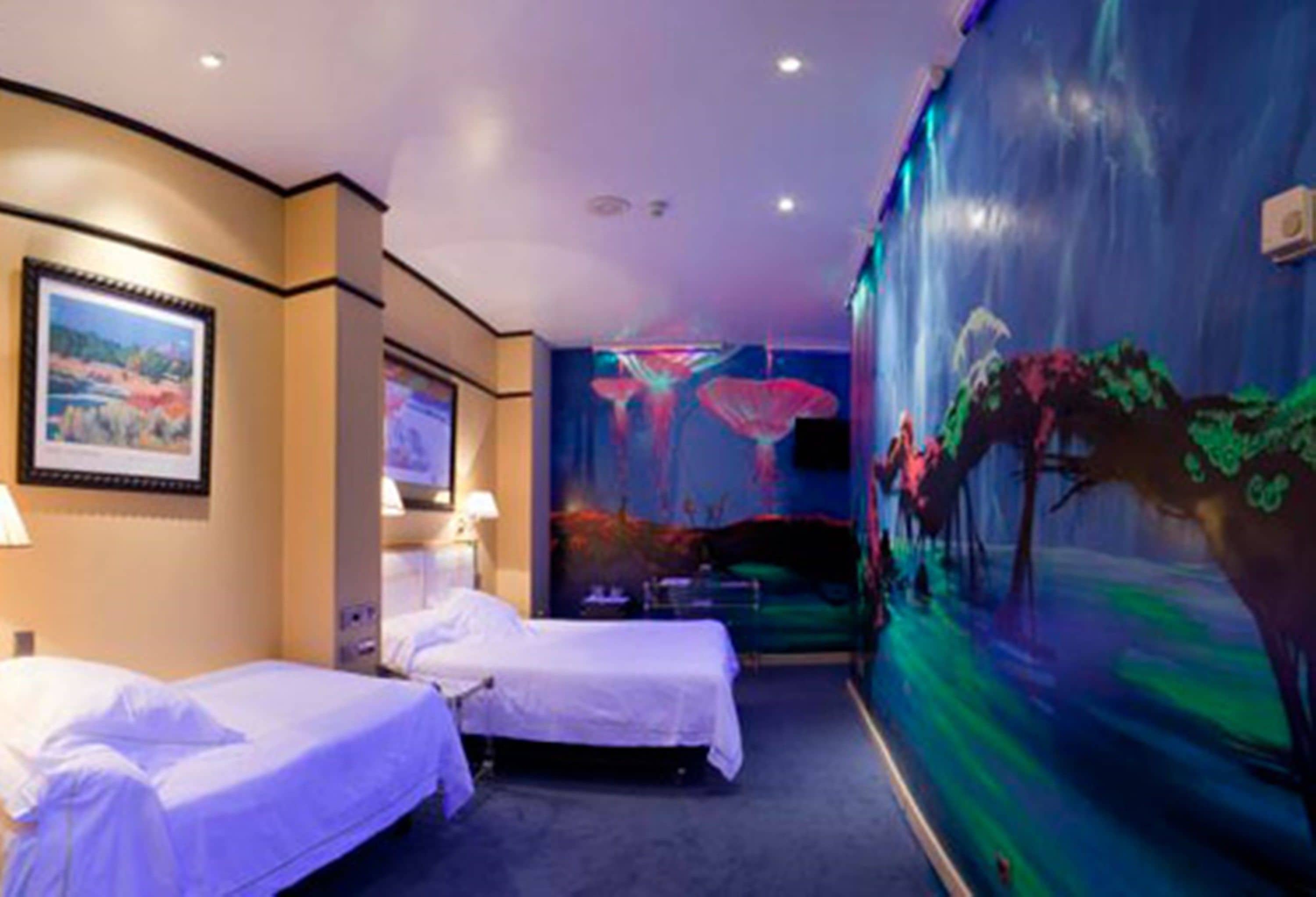 A hotel room with two beds, a large mural on the wall, and a painting above the beds.