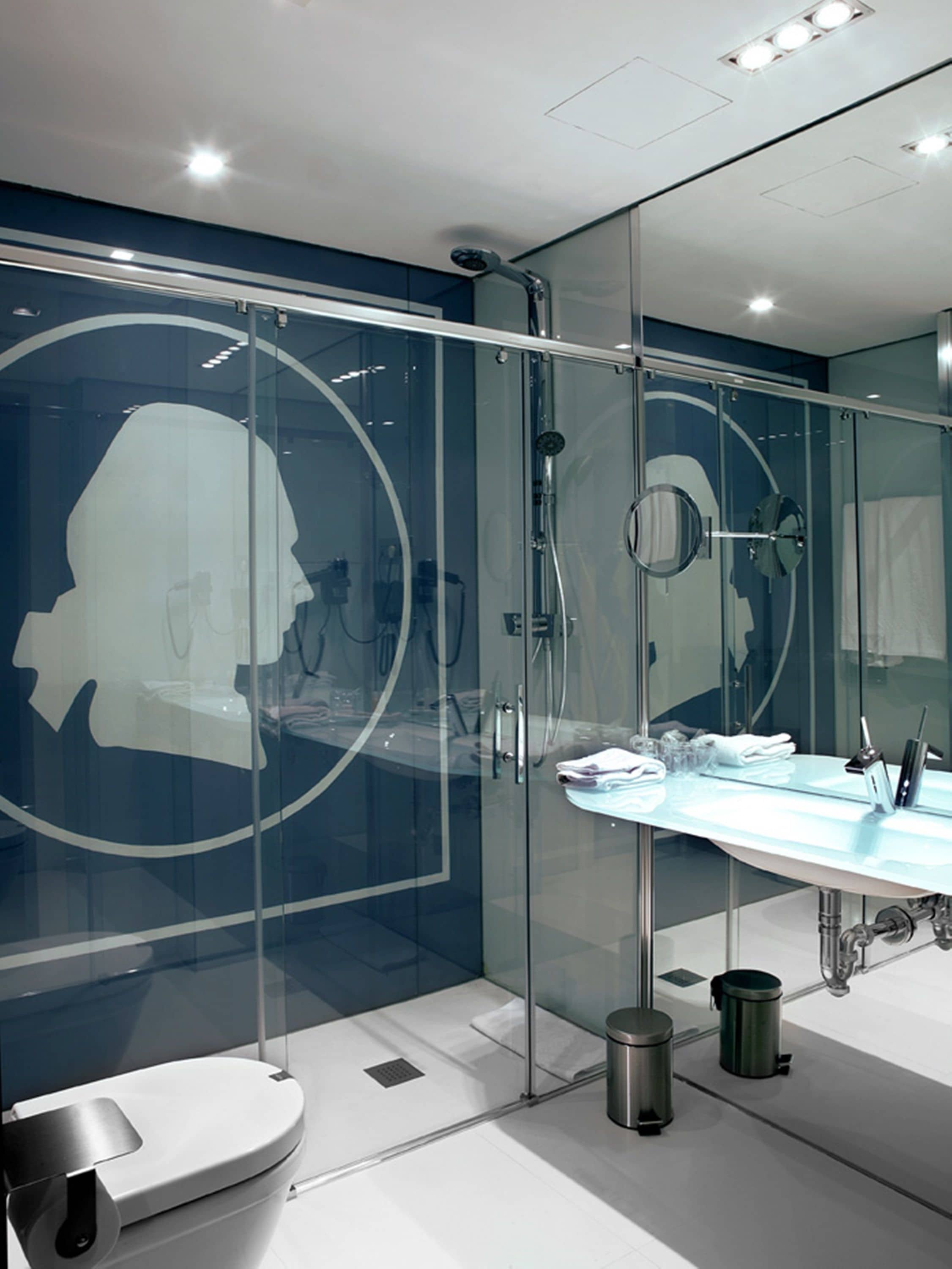 A modern bathroom with a glass shower enclosure, a white toilet, a sink with a mirror, and a trash bin.