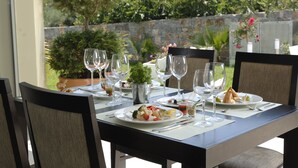 A dining table set for two with plates of food, wine glasses, and cutlery. - Angela Studios & Apartments (Agios Nikolaos)