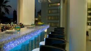 A bar area with a long counter, stools, and a decorative light fixture. - Angela Studios & Apartments (Agios Nikolaos)