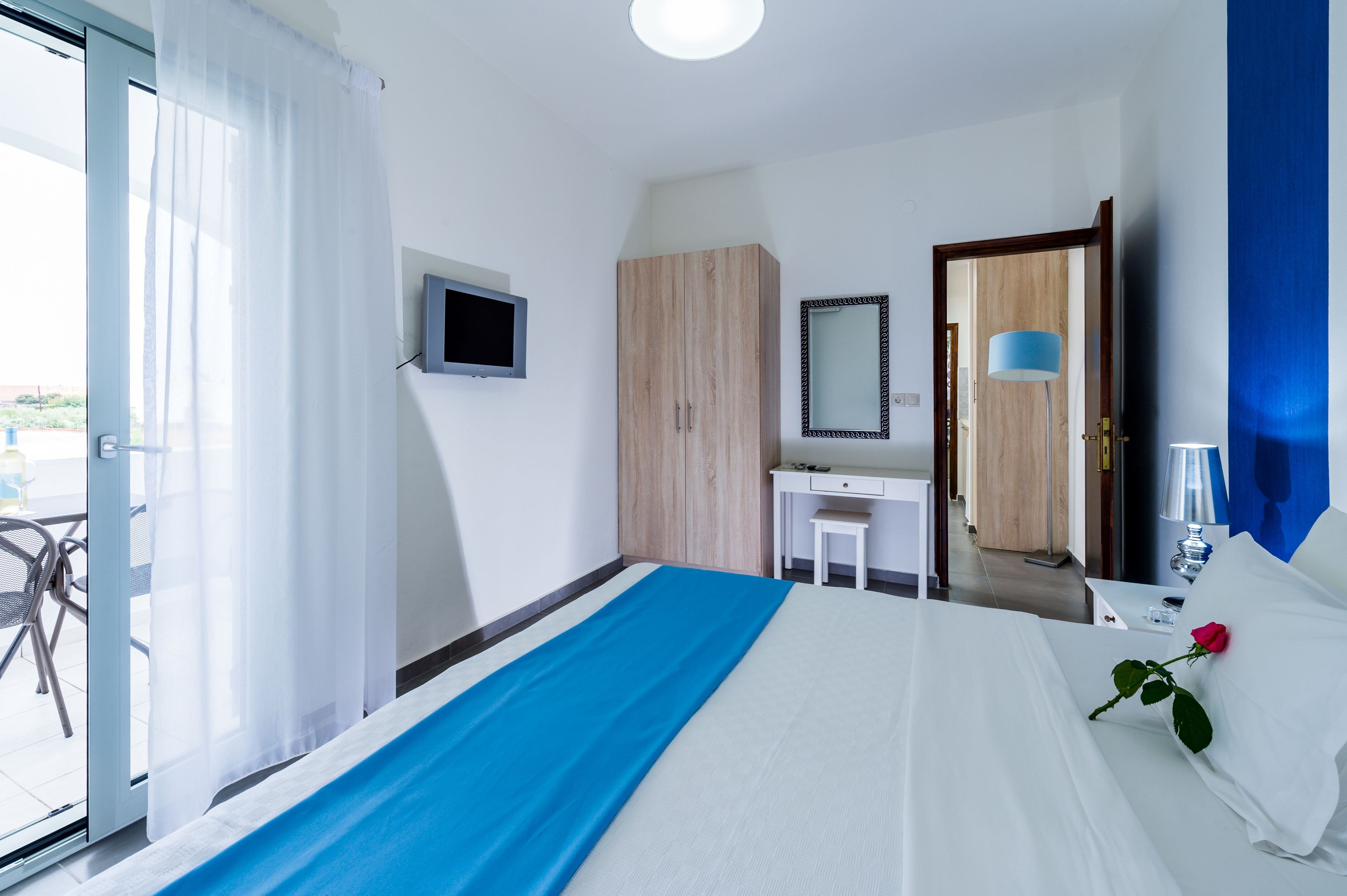 Habitación de hotel con cama, escritorio, espejo, televisor y vistas al exterior.