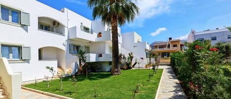 A modern residential building with a well-maintained garden and a clear blue sky.