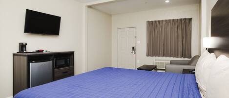 A hotel room with a large bed, a desk with a computer, a television, and a microwave.