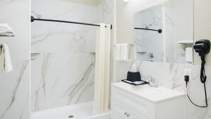 Un baño moderno con ducha de mármol, tocador blanco y secador de pelo.