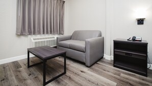 Una sala de estar con un sofá gris, una mesita pequeña, una mesita auxiliar de madera oscura y un teléfono instalado en la pared.