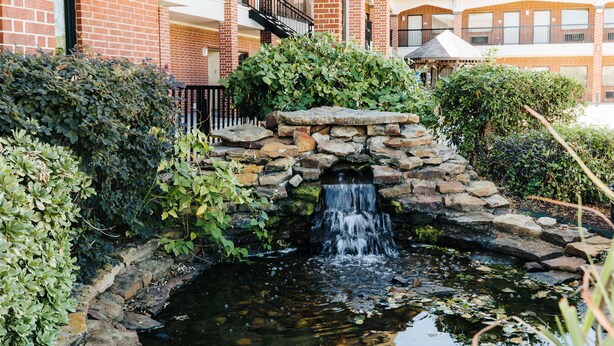 Una pequeña cascada en un patio con paredes de piedra y follaje.