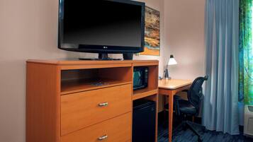 A hotel room with a flat-screen TV, a microwave, a mini fridge, a desk with a chair, and a window with curtains.