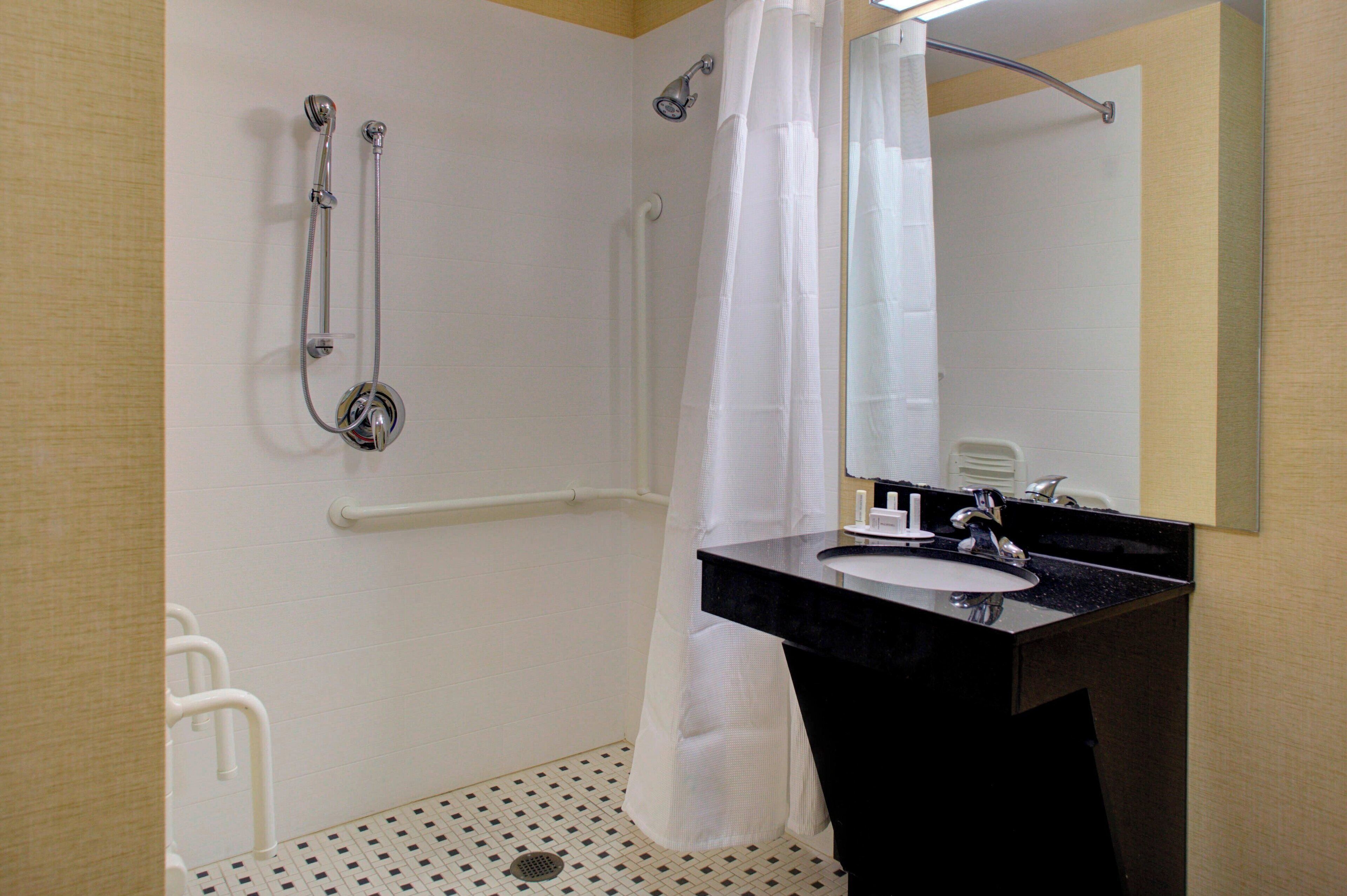 Ein Badezimmer mit einem schwarzen Waschbecken, weißen Wänden, einer Duschkabine mit Vorhang und einem Spiegel.
