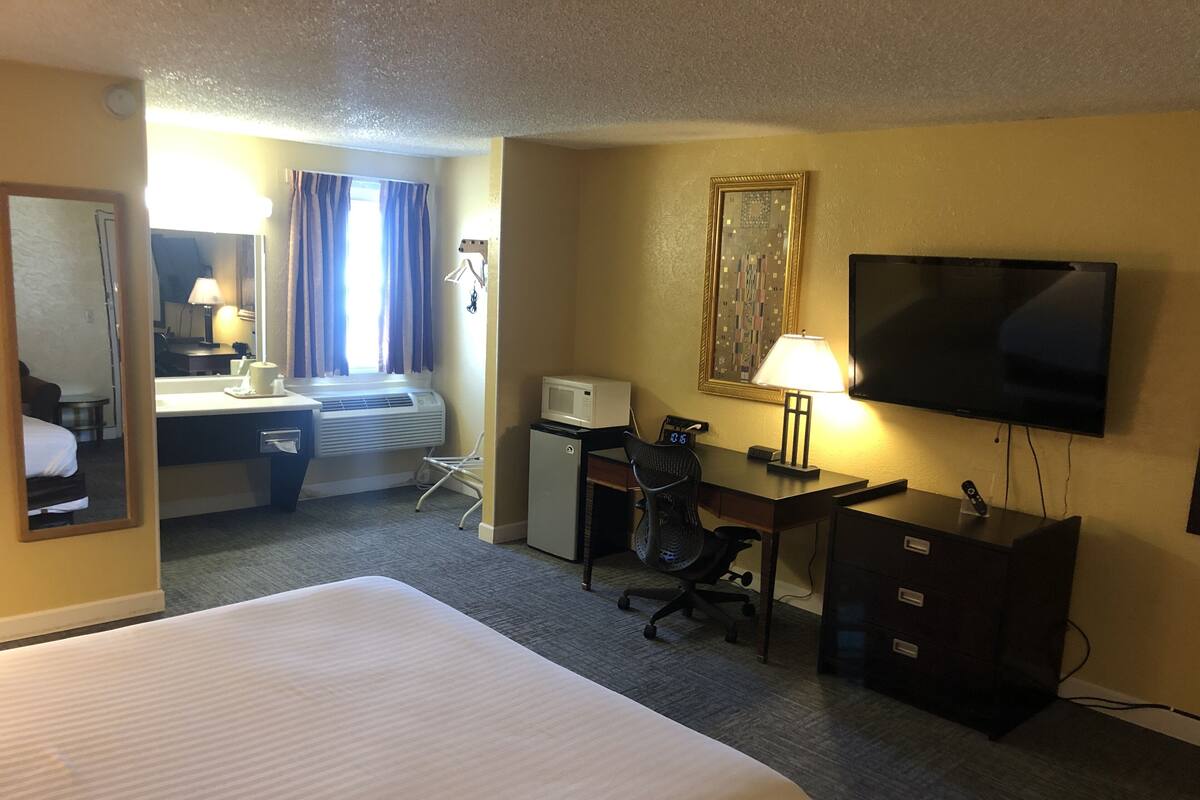 A hotel room with a bed, desk, chair, TV, and a small refrigerator.