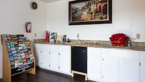 A kitchen with white cabinets, a small dishwasher, a fire extinguisher, a framed painting, and a welcome sign. - Nendels Inn & Suites (Dodge City)