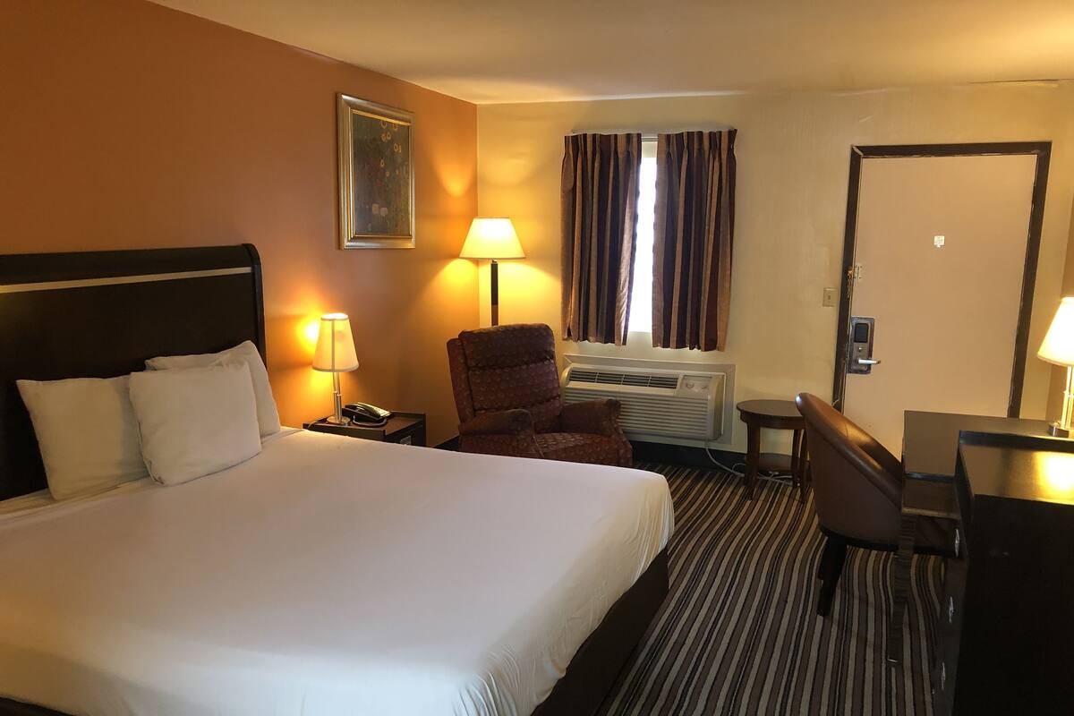 A hotel room with a large bed, a chair, a desk, and a window with curtains.