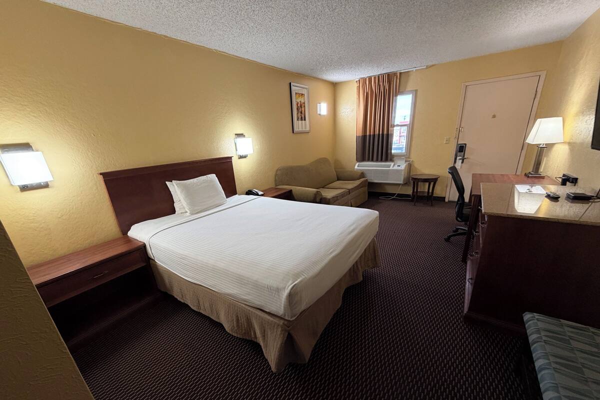 A hotel room with a large bed, a desk, a chair, a small table, and a couch.