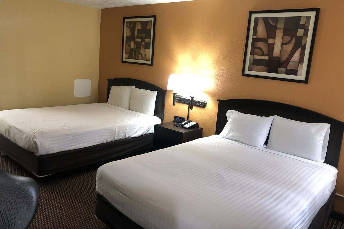 A hotel room with two beds, a nightstand with a lamp, and two framed artworks on the wall.