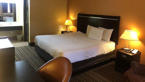 A hotel room with a bed, two bedside lamps, a desk, and a chair. - Nendels Inn & Suites (Dodge City)