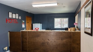 A hotel reception area with a wooden reception desk, a clock, framed certificates, and a window with bars. - Nendels Inn & Suites (Dodge City)