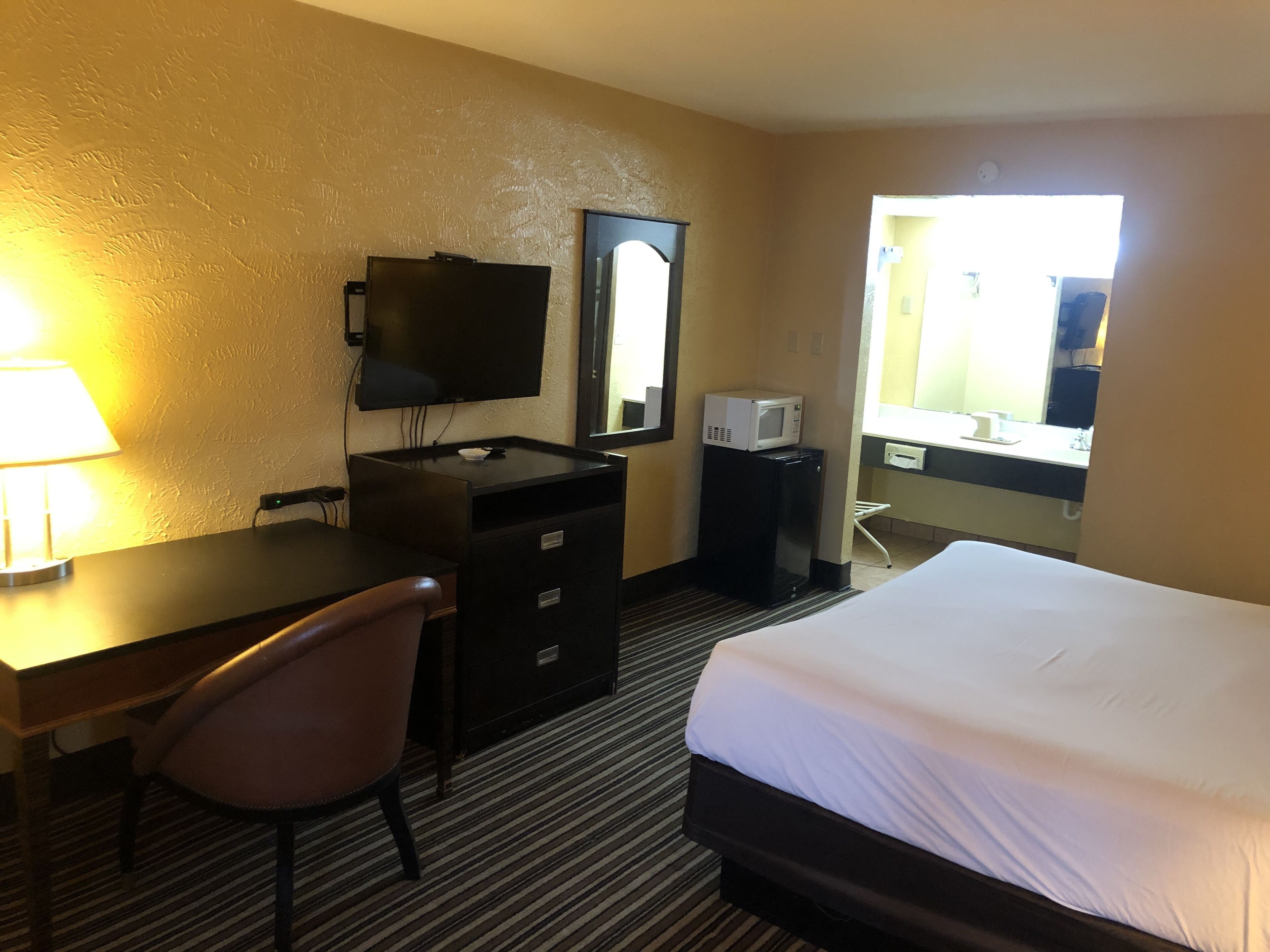 A hotel room with a bed, a desk with a chair, a television, a microwave, and a mirror.