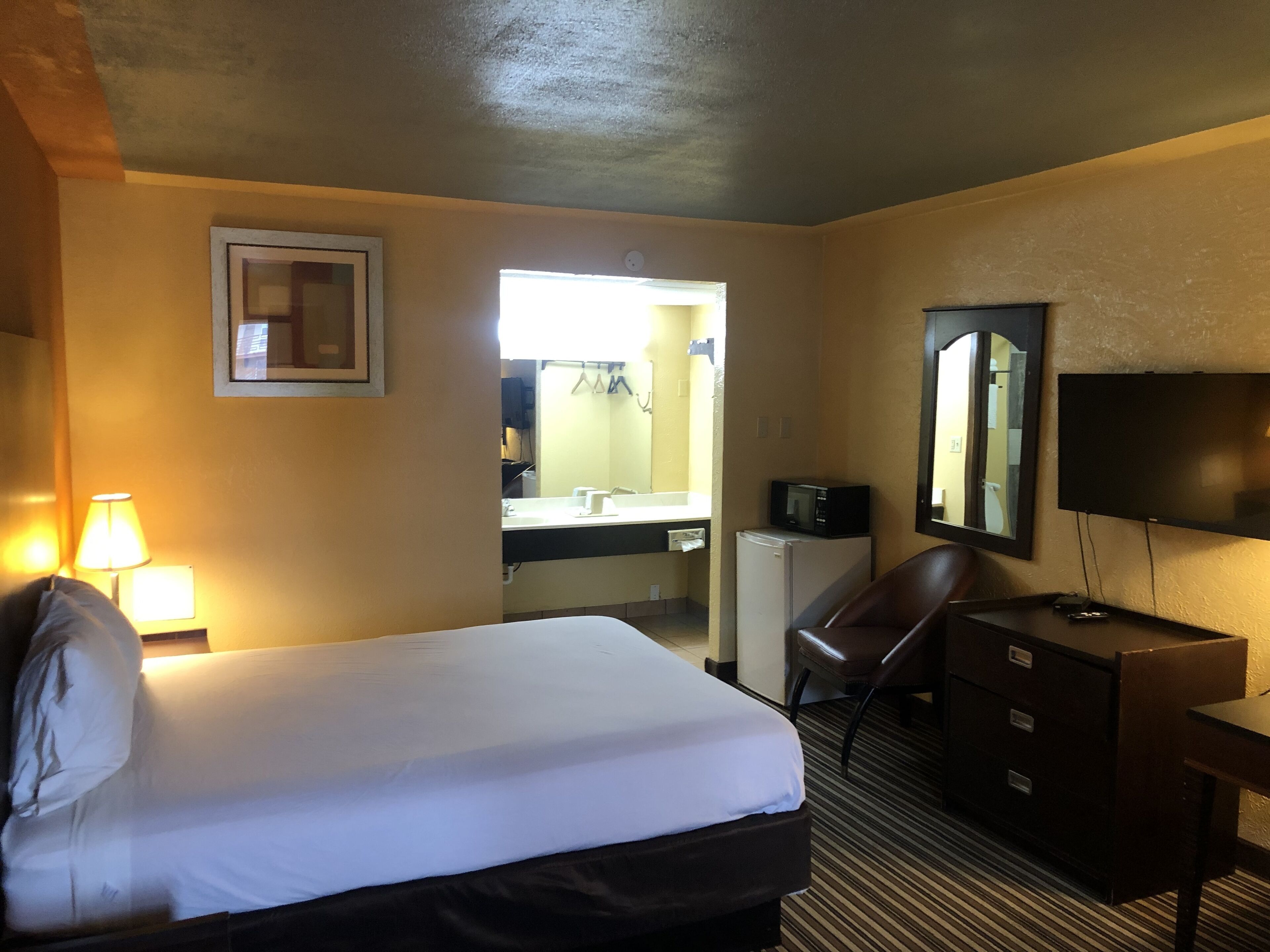 A hotel room with a bed, a desk, a chair, a TV, a microwave, and a mirror.