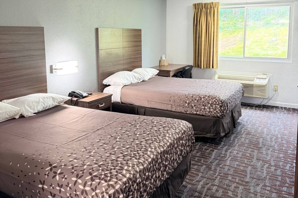 Habitación de hotel con dos camas, un escritorio, una silla, un teléfono y una ventana con cortinas.