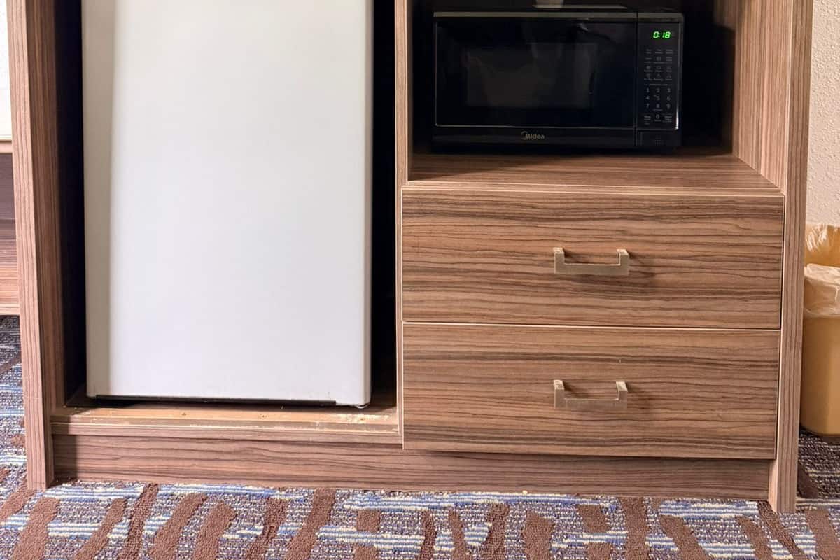 Una kitchenette compacta con refrigerador, microondas y televisor sobre un mueble de madera.