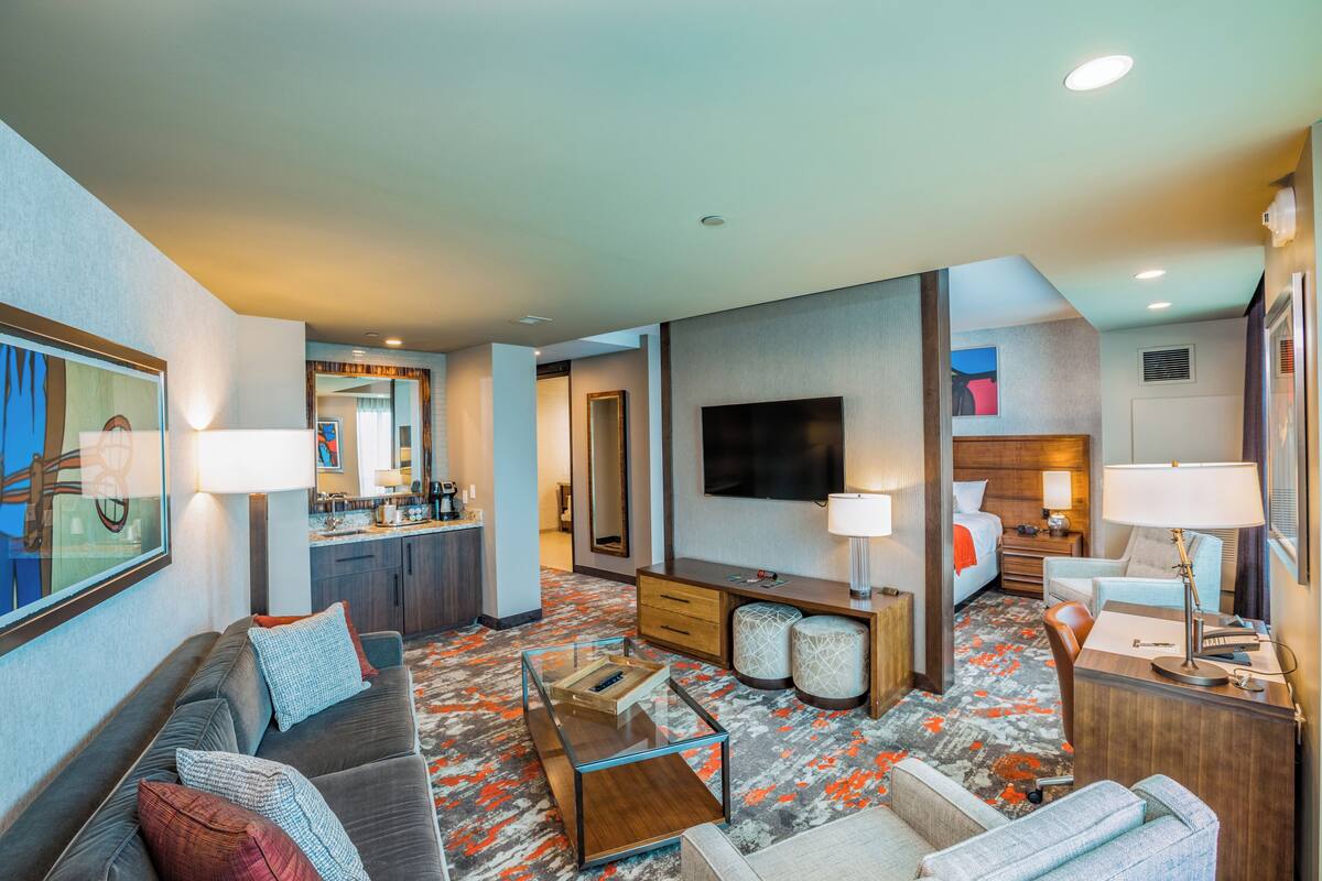 Habitación de hotel con sofá, sillón, escritorio, televisión y una kitchenette.