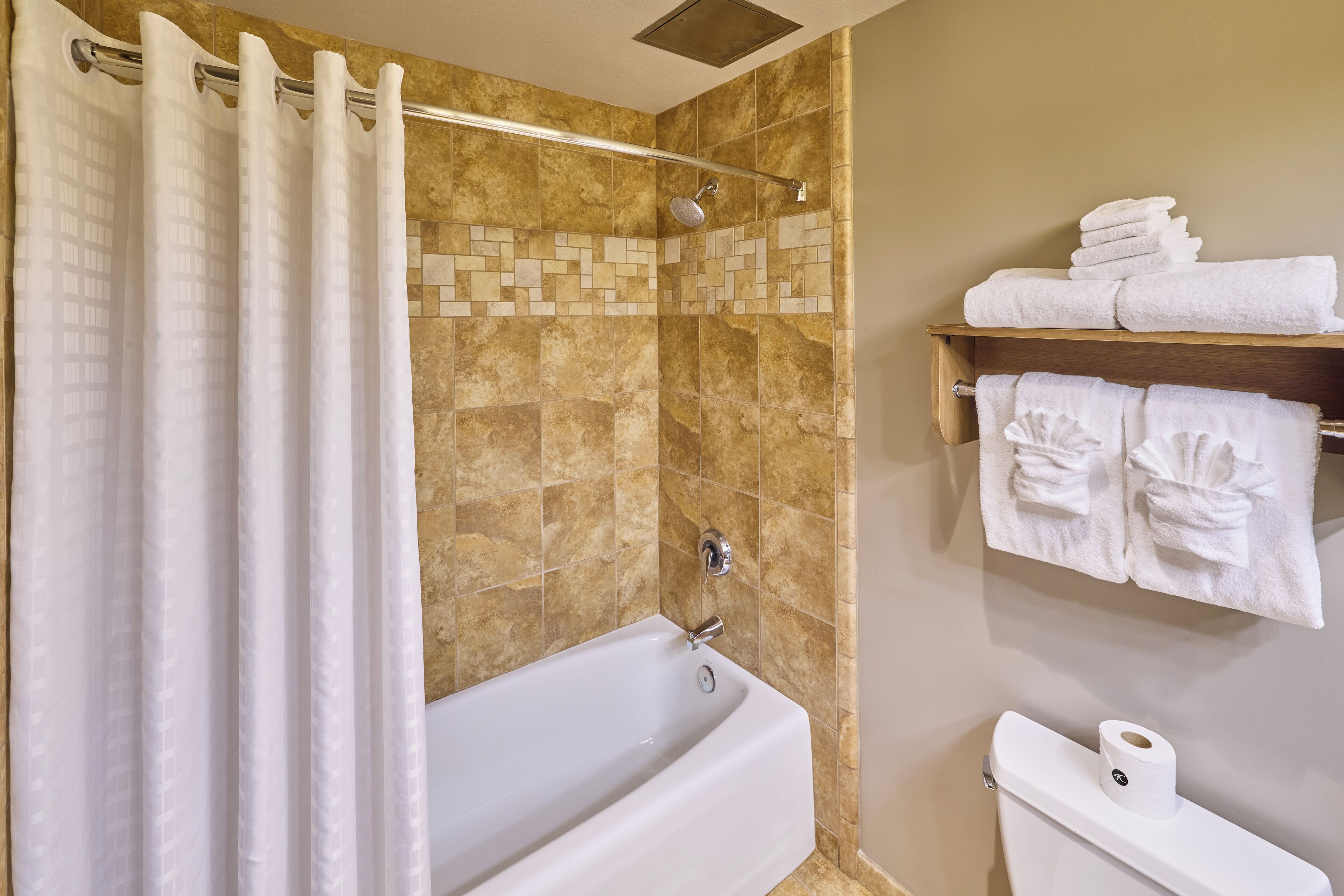 A bathroom with a bathtub, shower curtain, tiled walls, and towels on a shelf.