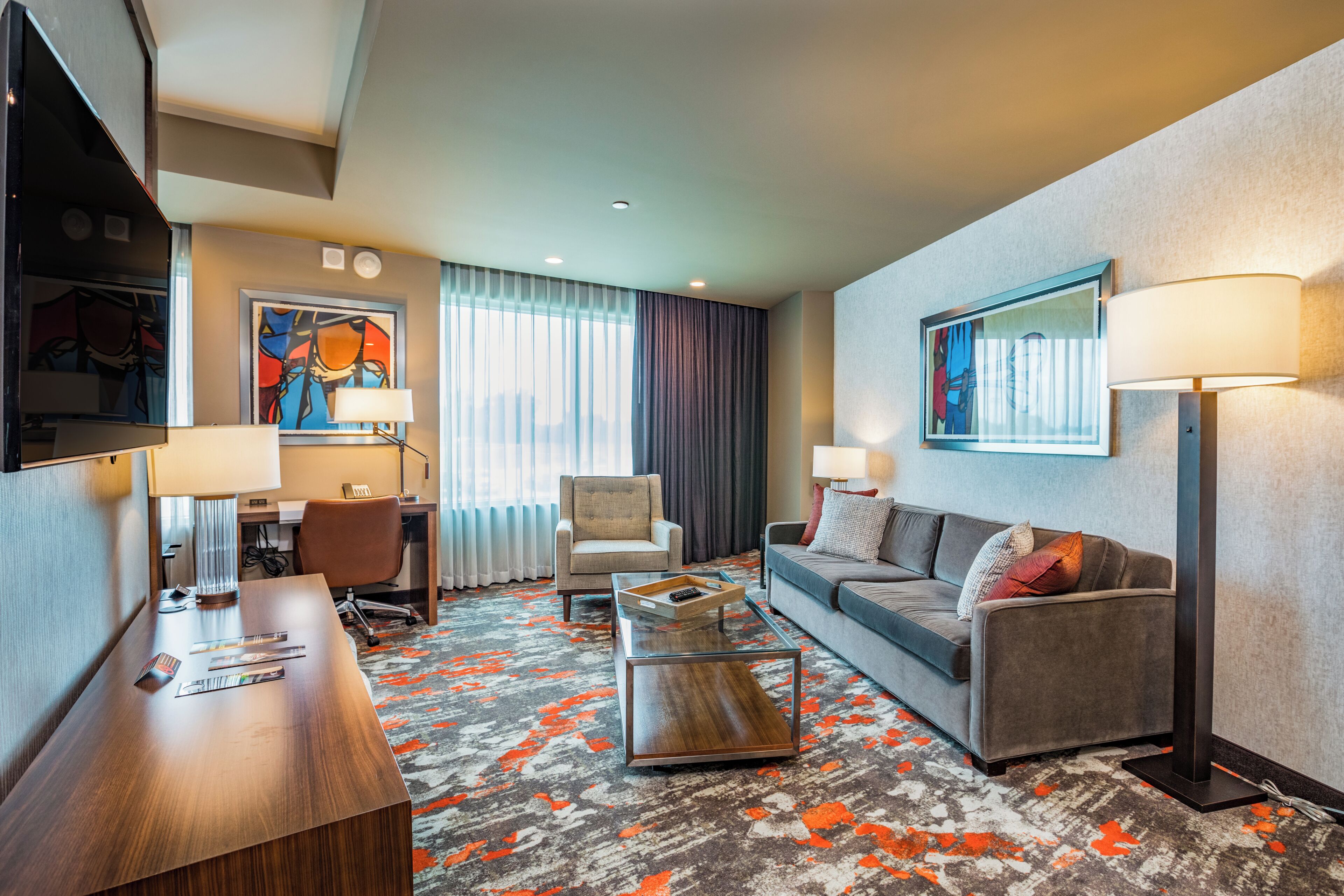 A hotel room with a desk, chair, sofa, and a large window.