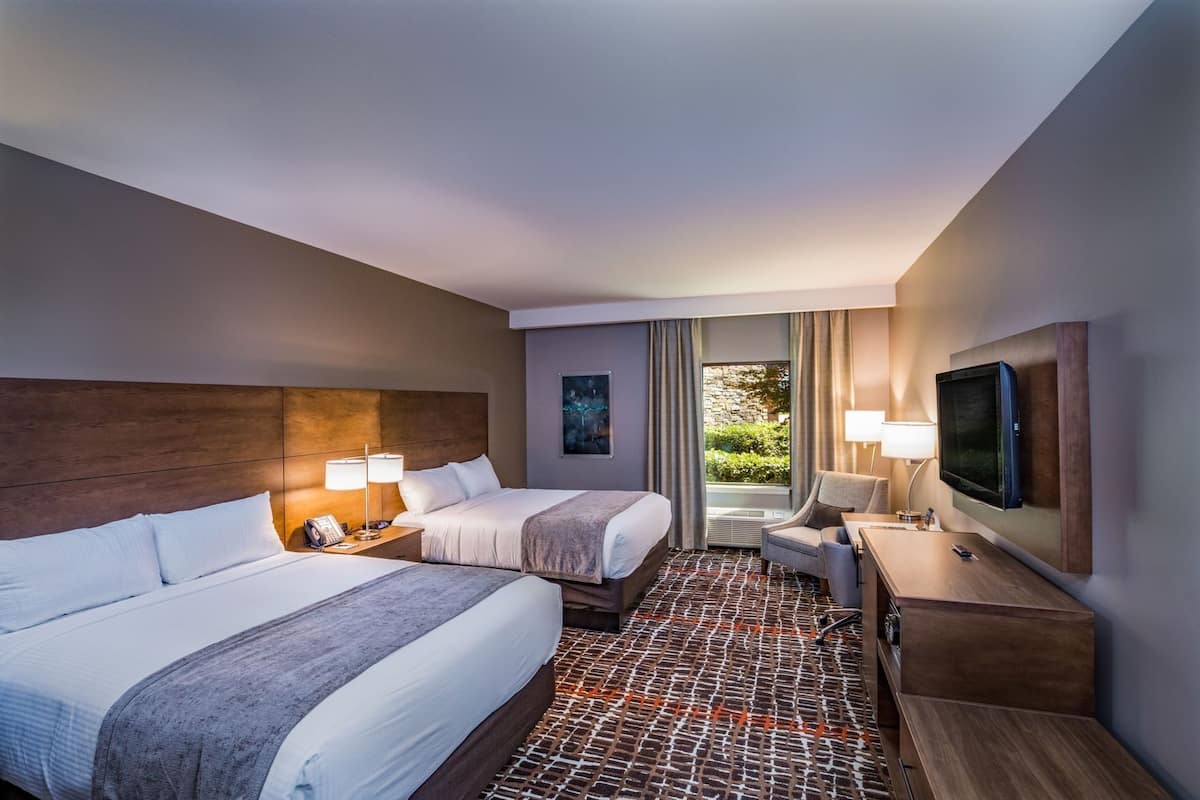 A hotel room with two beds, a desk, a chair, a TV, and a window with a view.