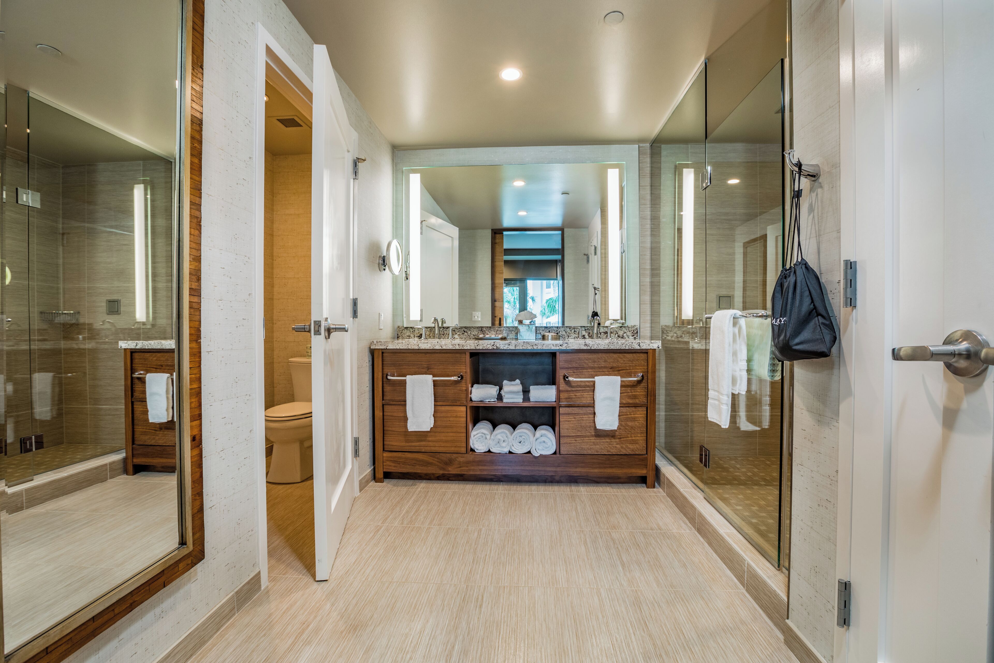 Un bagno moderno con cabina doccia in vetro, un mobile bagno in legno con piano in marmo e uno specchio grande.