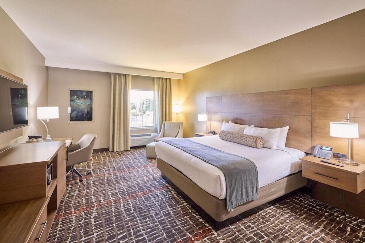 A hotel room with a bed, desk, chair, bedside tables, and artwork on the walls.