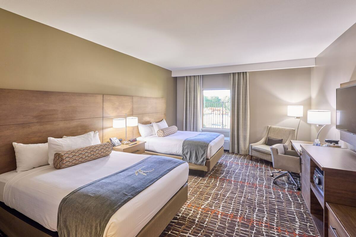 Habitación de hotel con dos camas, un escritorio, una silla, un televisor y una ventana con cortinas.