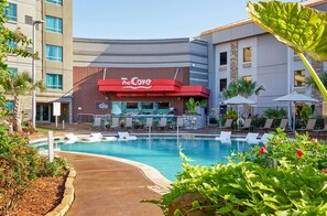 Un hotel con piscina, sillas de descanso y zona de bar.