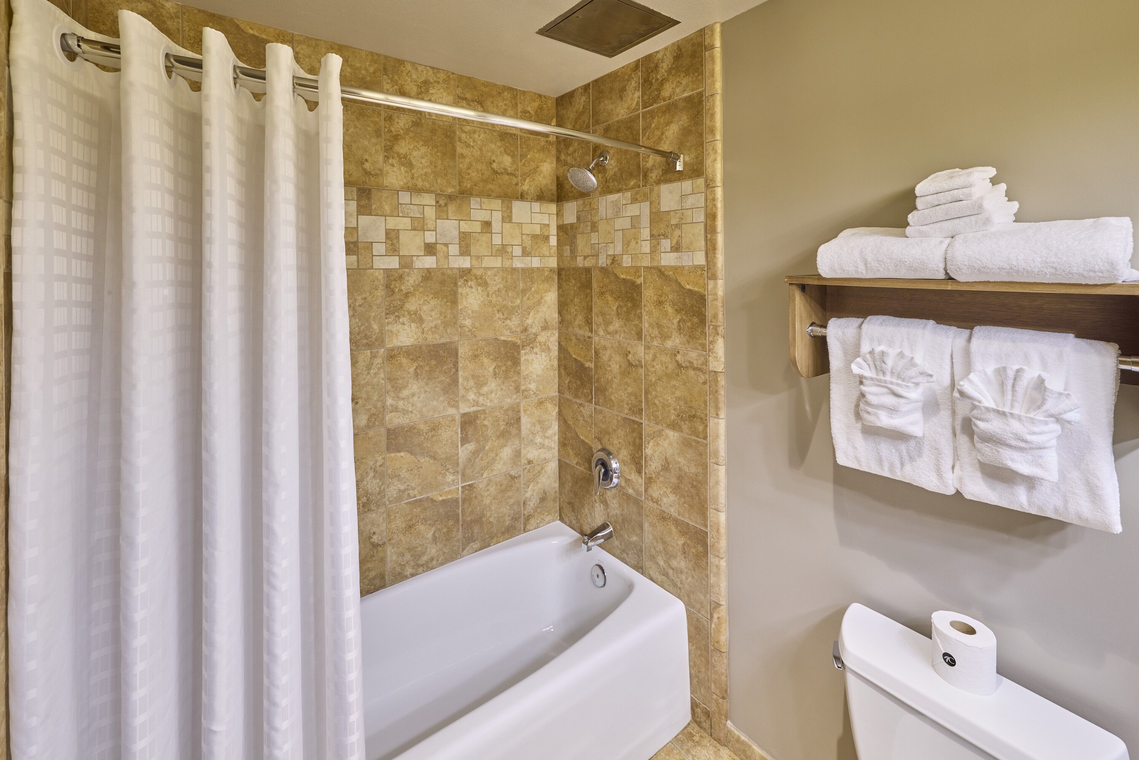 A bathroom with a bathtub, shower curtain, tiled walls, and towels on a shelf.