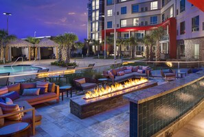 A poolside area with a fire feature, outdoor seating, and a modern building in the background. - Choctaw Casino & Resort Grant, Trademark Collection by Wyndham (Grant)
