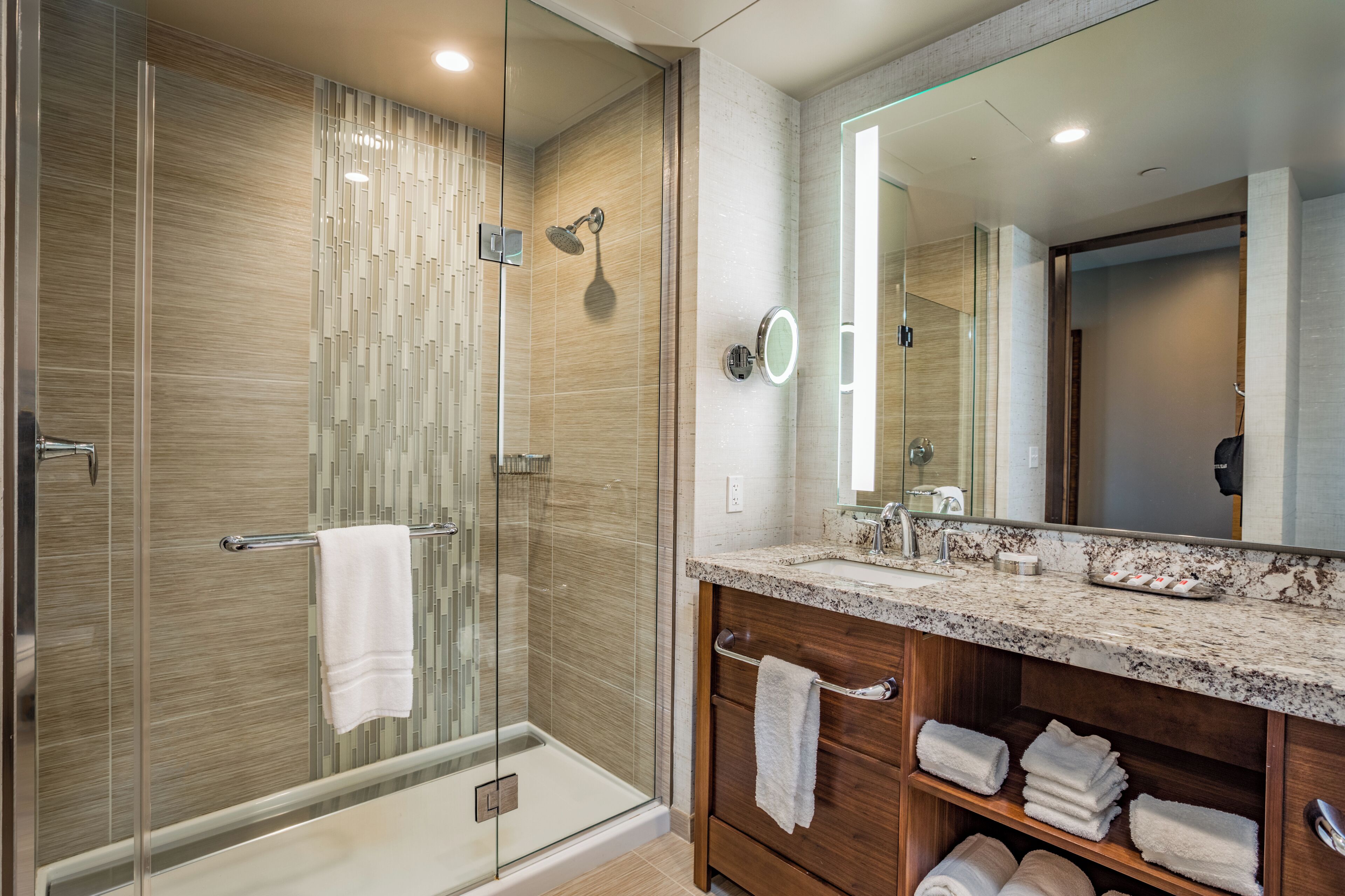 A modern bathroom with a glass-enclosed shower, a vanity with a marble countertop, and a large mirror.