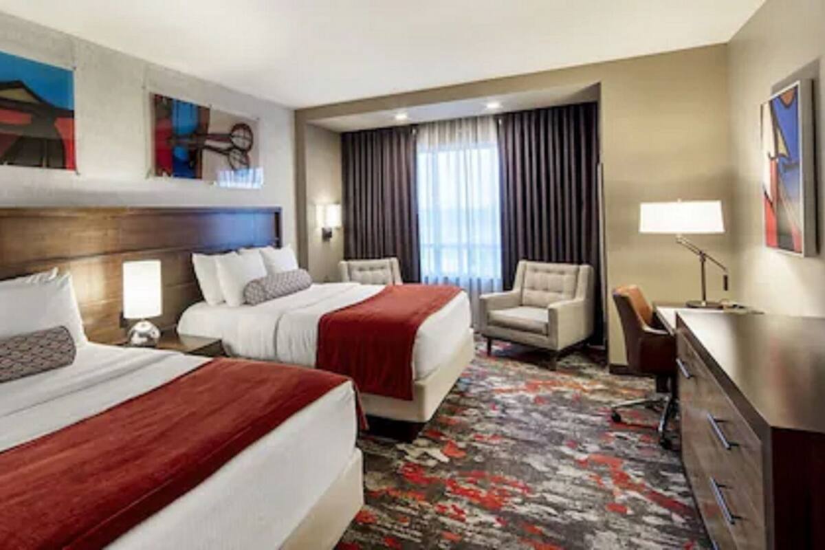 A hotel room with two beds, a desk, a chair, and a large window with curtains.
