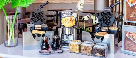 A breakfast bar with waffle makers, condiments, and a waffle display.