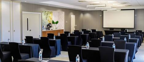 A conference room with rows of tables, chairs, and a projector screen.