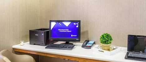 Un espace de travail dans une chambre d’hôtel, comprenant un bureau, un ordinateur, un téléphone et une petite plante.