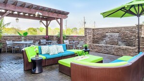 An outdoor patio area with a wooden pergola, stone wall, and seating arrangements including a sofa and chairs. - SpringHill Suites Houston NASA/Seabrook (Seabrook)