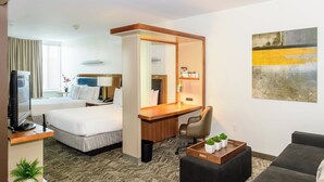 A hotel room with a bed, a desk, a chair, a TV, a coffee table with plants, and a painting on the wall. - SpringHill Suites Houston NASA/Seabrook (Seabrook)