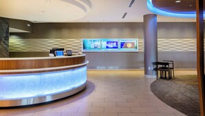 A hotel reception area with a curved reception desk, a digital information display, and a seating area with a table and chairs. - SpringHill Suites Houston NASA/Seabrook (Seabrook)