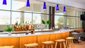 A bar area with wooden stools, a variety of bottles, and a large window with blue pendant lights. - SpringHill Suites Houston NASA/Seabrook (Seabrook)