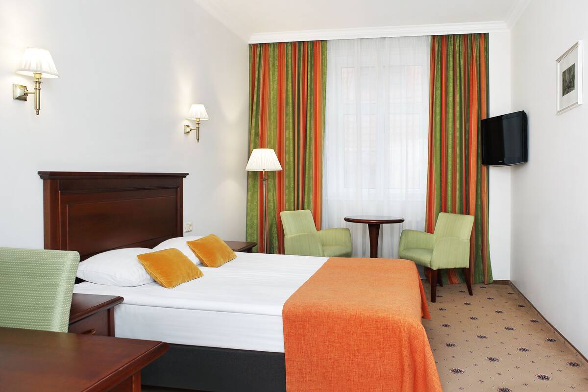 A hotel room with a bed, two chairs, a small table, a TV, and curtains.