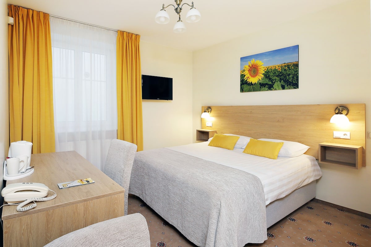A hotel room with a bed, bedside lamps, a TV, a coffee maker, and a telephone.