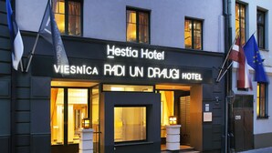 Entrada de un hotel con un cartel que dice "Hestia Hotel VIESNICA RADI UN DRAUGI HOTEL" y banderas de la Unión Europea y Eslovenia.